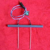 Blue handheld zapper device with copper handles and wire on red textured background