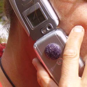 Hand holding a small electronic device with LCD display and buttons, with a dark round object (possibly orgonite) visible