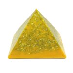 Gelbe orgonite-Pyramide mit Metallspänen in durchscheinendem Harz, von vorne gegen weißen Hintergrund fotografiert