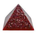 Pyramide orgonite rouge translucide avec copeaux métalliques et spirales de cuivre incorporés, photographiée sur fond blanc