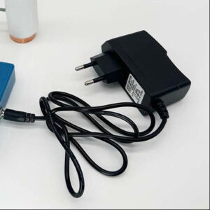 Black power adapter with two-prong European plug and attached black cable with connector end on white surface