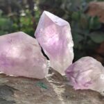 Trois morceaux de cristal d'améthyste violet translucide sur surface de pierre patinée, éclairage naturel extérieur
