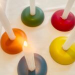 Fünf bunte runde orgonite Kerzenhalter mit weißen Kerzen - grün, rot, orange, gelb und dunkelblau/lila auf weißer Oberfläche