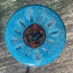 Kreisförmige blaue orgonite Scheibe mit metallischer Spiralspule in der Mitte und Kristallsplittern, von oben auf Gewebe