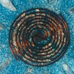 Dunkle Spiralspule mit metallischen kupferfarbenen Kanten auf zerkleinertem blauen Kristallhintergrund mit klaren Kristallspitzen