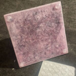 Baldosa cuadrada de orgonite rosa con superficie rugosa y elementos circulares transparentes en esquinas, junto a molde blanco