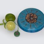 Blaue runde orgonite-Scheibe mit Kupferspirale in der Mitte und Strahlenlinien, neben Limettenhälften und grünem Baumanhänger