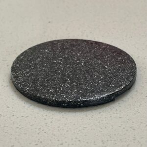 Disque circulaire gris foncé avec texture de surface rugueuse et tachetée sur fond blanc moucheté