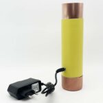 Appareil cylindrique jaune avec extrémités métalliques cuivrées et adaptateur secteur noir avec câble sur fond blanc
