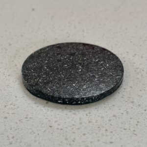 Black circular disc with metallic speckled surface texture on white speckled background, viewed from above