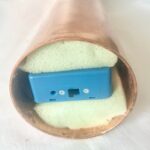 Appareil électronique bleu avec composants métalliques dans mousse blanche à l'intérieur d'un bâton orgonite cuivré