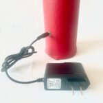 Baguette orgonite cylindrique rouge à surface texturée reliée à un adaptateur secteur noir par câble, vue de côté
