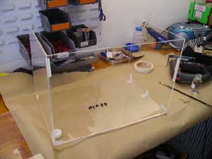 Clear acrylic display case or container on wooden surface in cluttered workshop or storage room with boxes and equipment