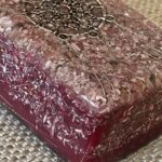 Rechteckiger lila-roter Harzblock mit eingebetteten Metallspiralen und Kristallsplittern auf gewebter Matte