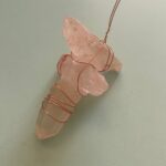 Pink crystal stones wrapped in copper wire against white background, pendant-style jewelry piece