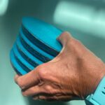 Hand hält Stapel blauer runder Scheiben mit dunklen Schichten dazwischen, Poolwasser unscharf im Hintergrund