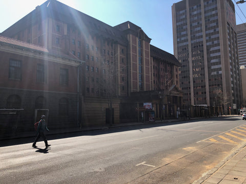 Street scene with historic stone building on left, modern high-rise on right, person walking, bright sunlight creating lens flare