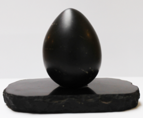Black polished egg-shaped stone object sitting on a black oval base against white background