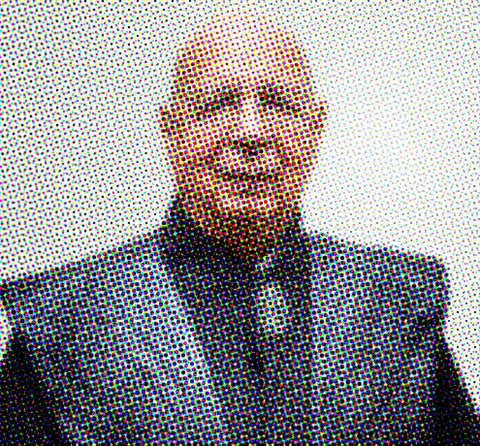 Pixelated portrait of a smiling bald man in dark clothing against a light background
