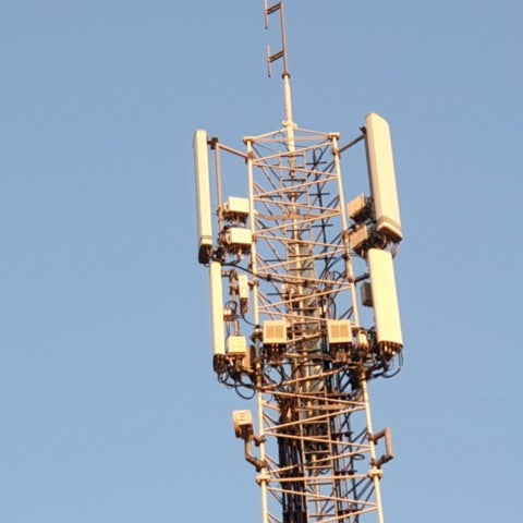 Tall cellular phone tower with multiple antenna arrays and equipment mounted on metal lattice structure against blue sky