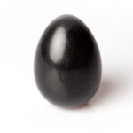 Black polished shungite egg-shaped stone with glossy reflective surface, standing upright against white background