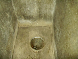 Concrete shower stall with drain hole in floor, water-stained walls in institutional setting