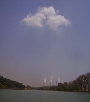 Lake scene with purple-tinted sky, white clouds above, industrial cooling towers visible in distance across water