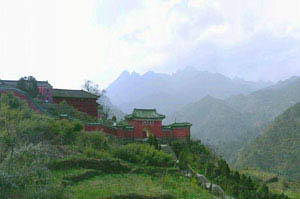 Red traditional buildings on terraced hillside with green vegetation, misty mountains in background