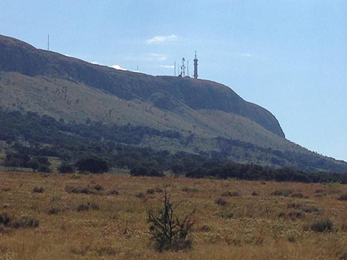 Hill with communication towers on summit, golden grassland in foreground, clear blue sky