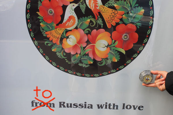 Decorative Russian folk art plate with floral design and bird, hand holding small object, text "to from Russia with love"