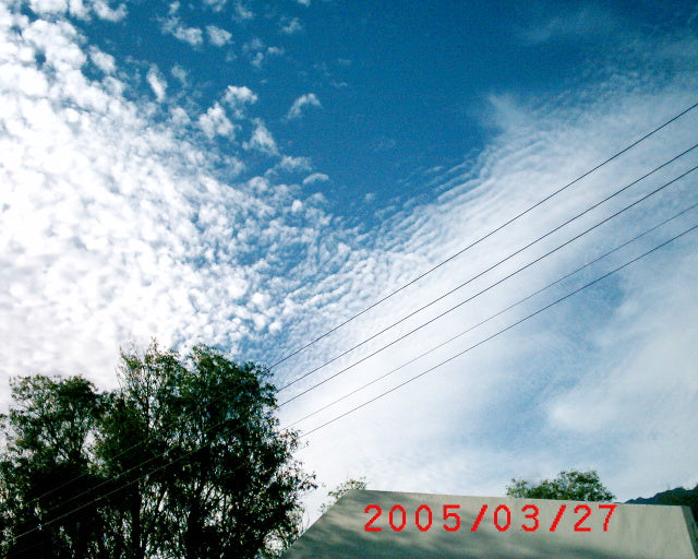 Blue sky with white puffy clouds, power lines crossing diagonally, green trees below, dated 2005/03/27