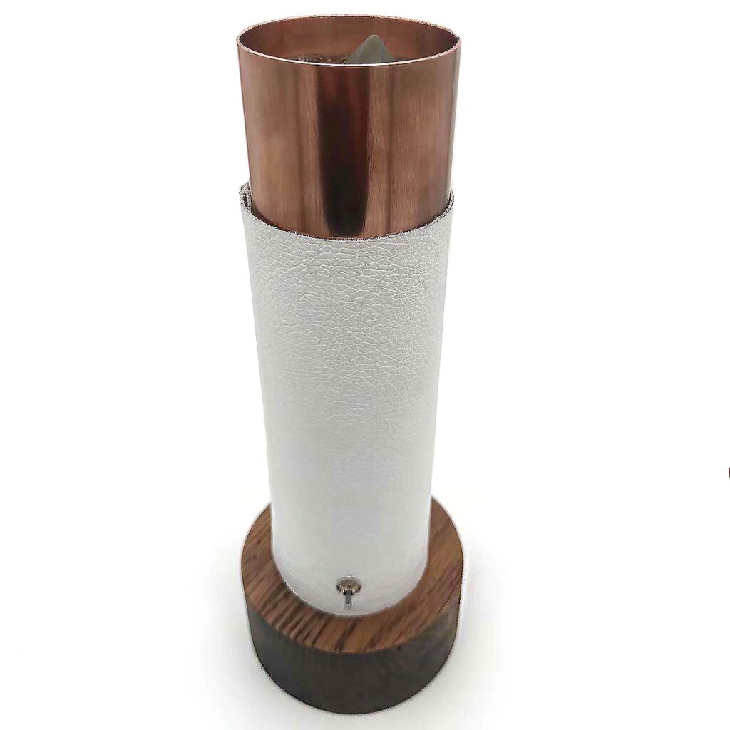 Tall cylindrical device with copper-colored top section, white textured middle section, and dark wooden base with small knob