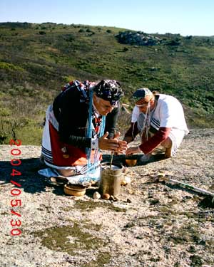 Zanemvula stirring a greenish liquid in an iron pot with a forked twig.